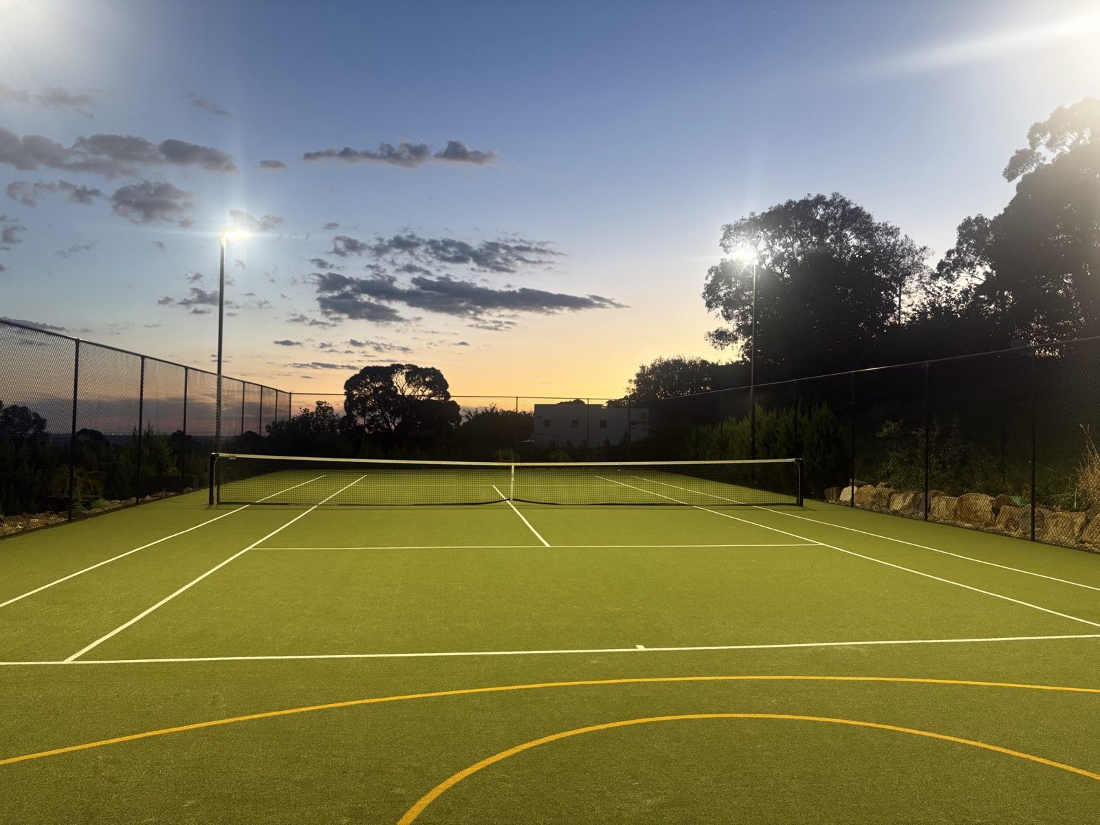 The floodlit tennis court at dusk, ready for a duo lesson